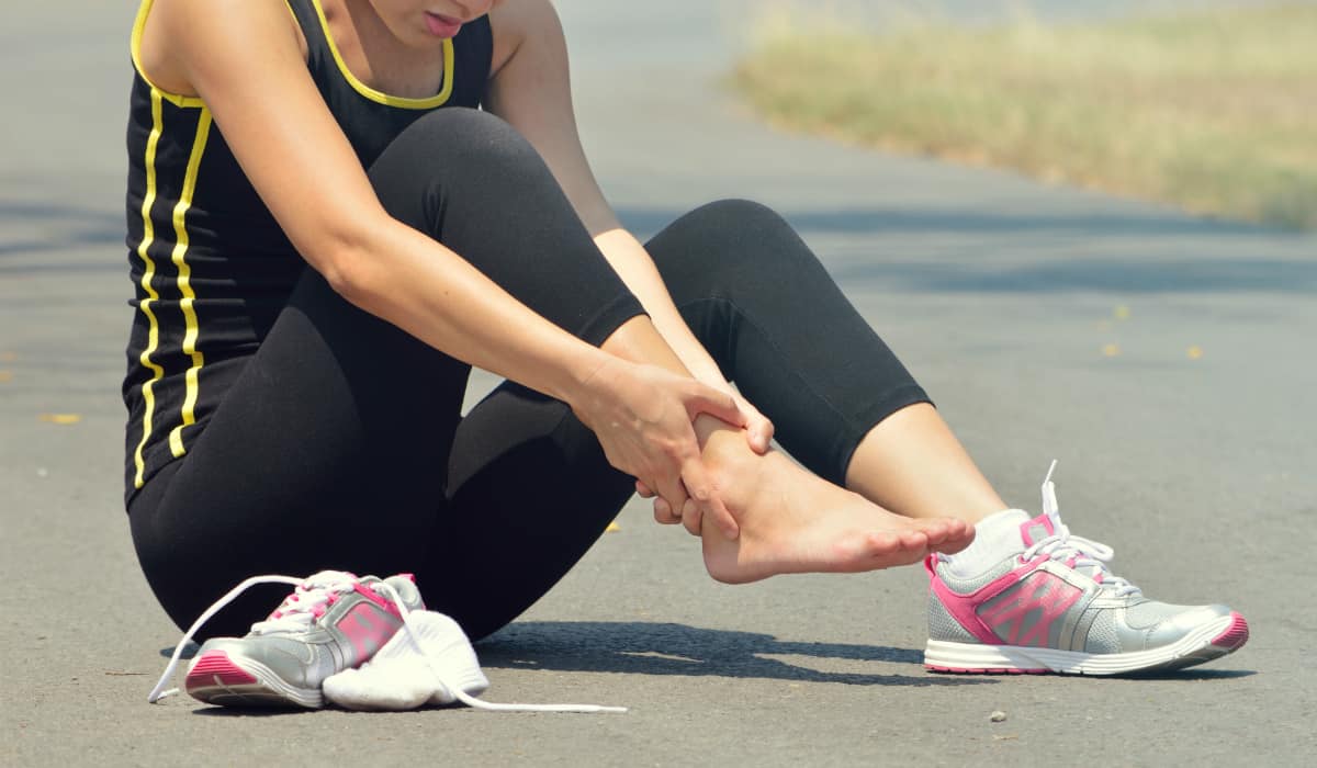 Athletic woman sitting on the ground with ankle pain
